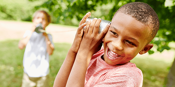 Two boys playing telephone with tin cans and string. 