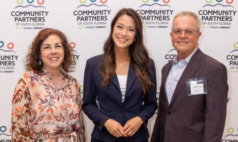 three adults stand in front of step and repeat